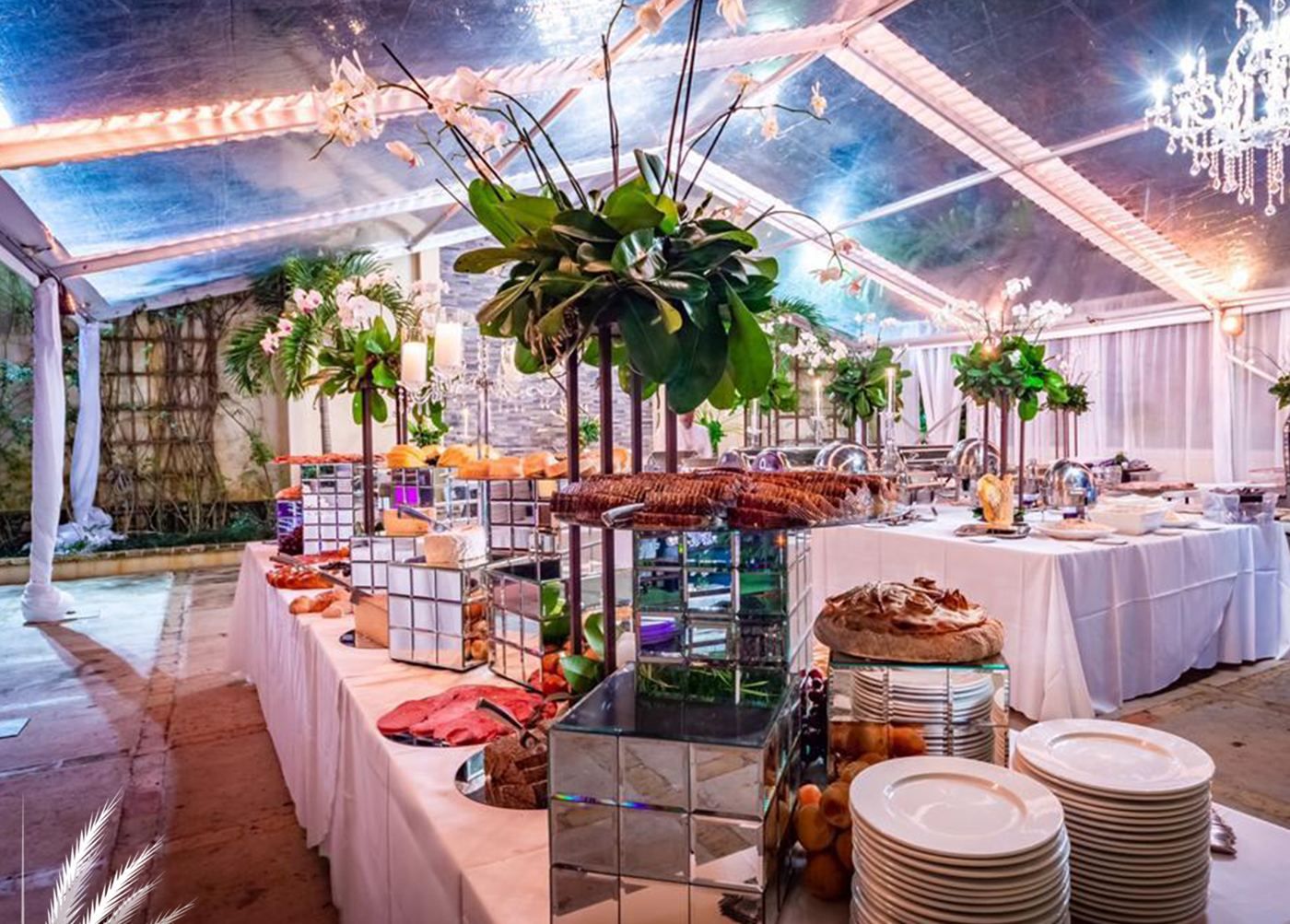 Buffet under a clear tent with tall greenery arrangements