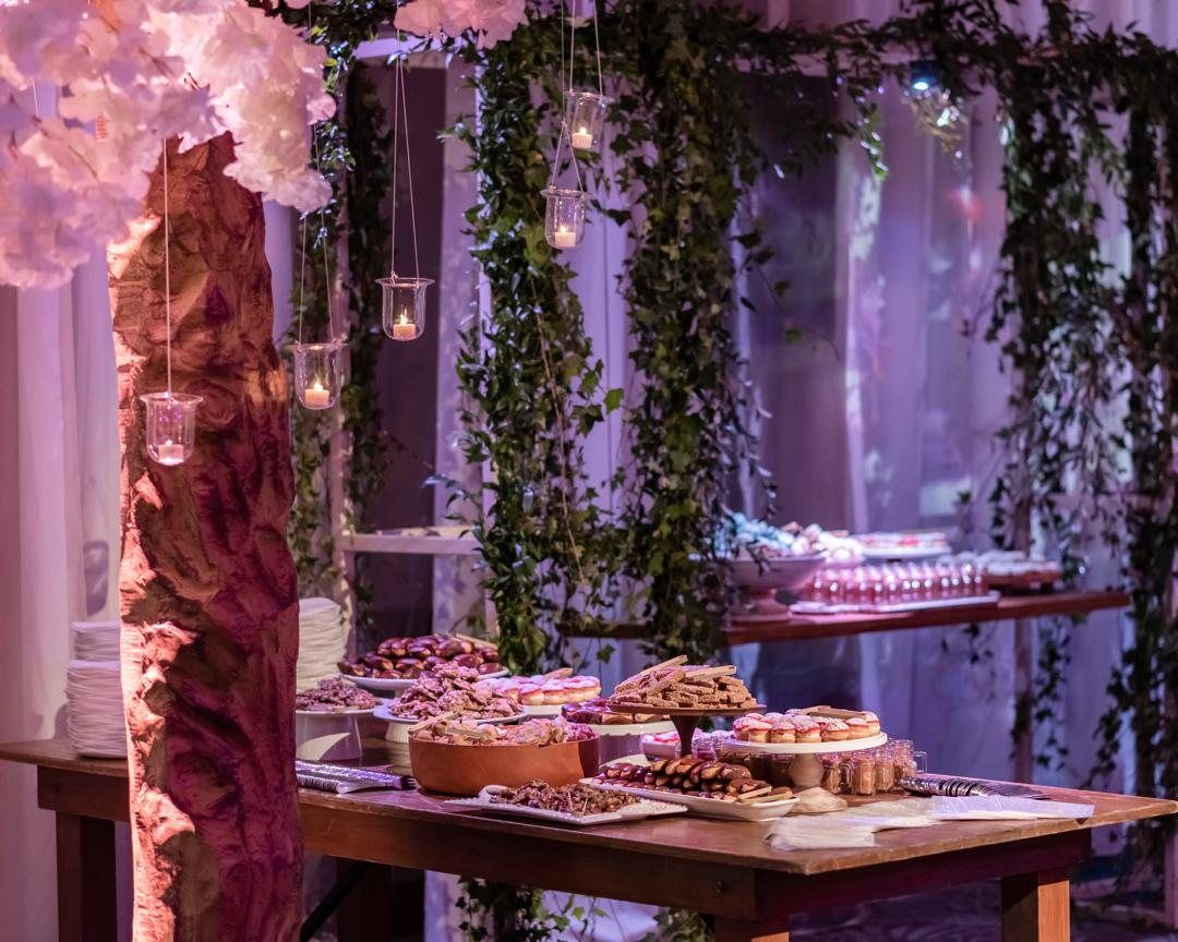 Dessert table beneath hanging candles and greenery in purple light