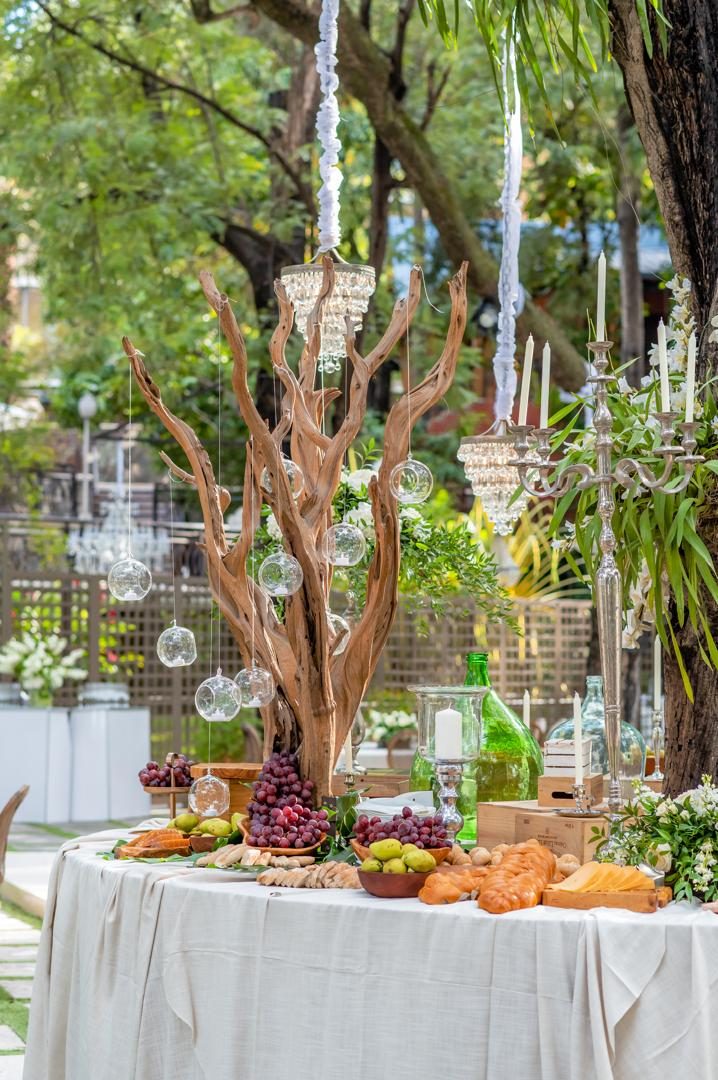 Grazing table with grapes, bread and cheese beneath a driftwood tree hung with glass orbs and chandeliers
